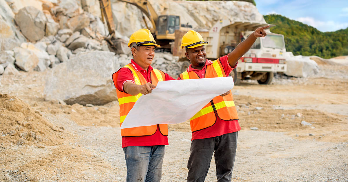 Two Sunway construction workers looking over the blueprint, with heavy equipment in the background