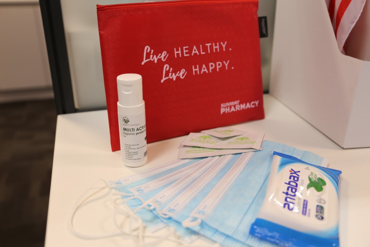 A medium close up of the Sunway safety kit with the pouch propped up, its contents spread out - of a bottle of hand sanitiser, couple of alcohol swabs and surgical masks fanned out alongside a pack of antibacterial wipes, on a white tabletop