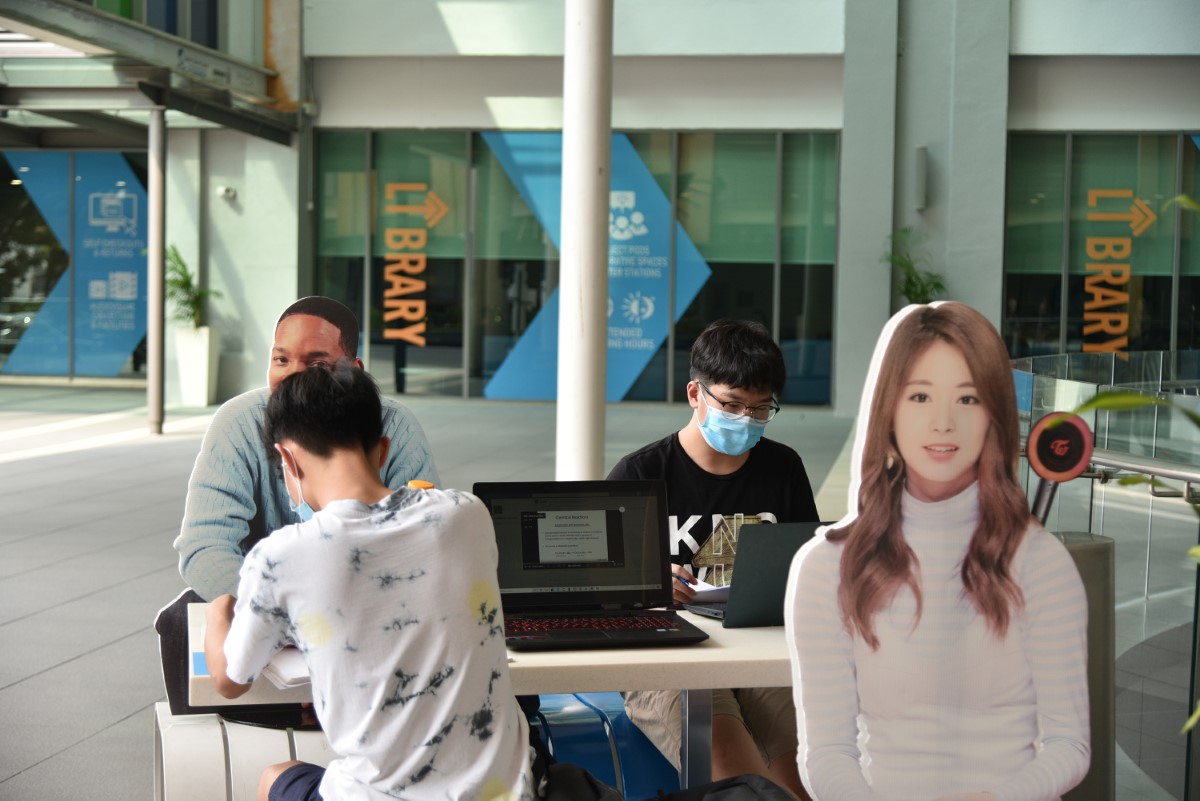 Students in face masks utilising the communal rest area within campus in compliance with SOP, featuring life-size cardboard cutouts of Twice’s Tzuyu and Will Smith
