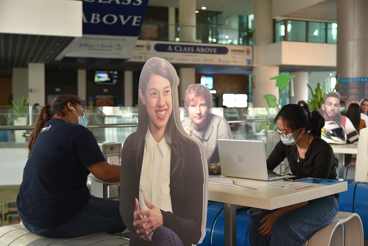 Students in face masks utilising the communal rest area within campus in compliance with SOP, featuring life-size cardboard cutouts of Dato Nicol Ann David and Ed Sheeran