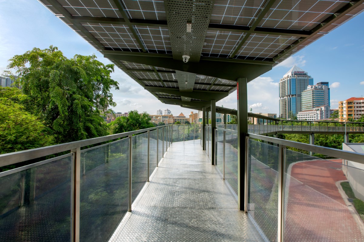 A wide-shot of Sunway’s Eco-Walk during daytime, with lush greeneries on the left and urban cityscape with more pedestrian tracks on the right