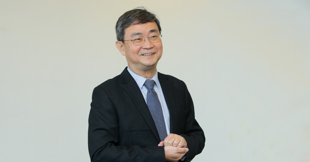 A mid-shot of a smiling Mr. Ong Pang Yen dressed smartly in a suit, facing away from the camera with his hands firmly clasped together.