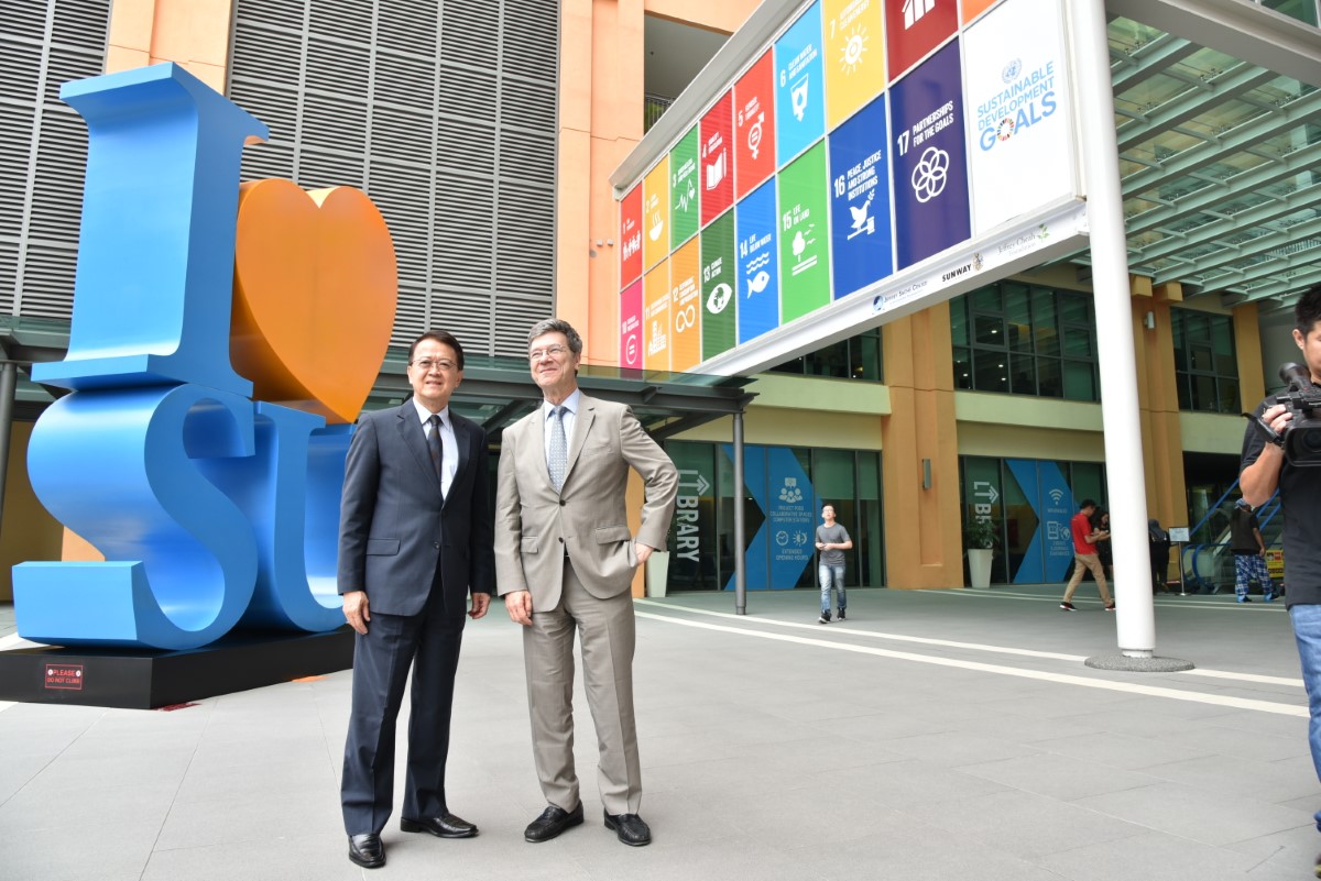 A wide shot of Tan Sri Dr. Jeffrey Cheah and Jeffrey David Sachs in front of the I Love Sunway and UN-SDG signboard at Sunway University.
