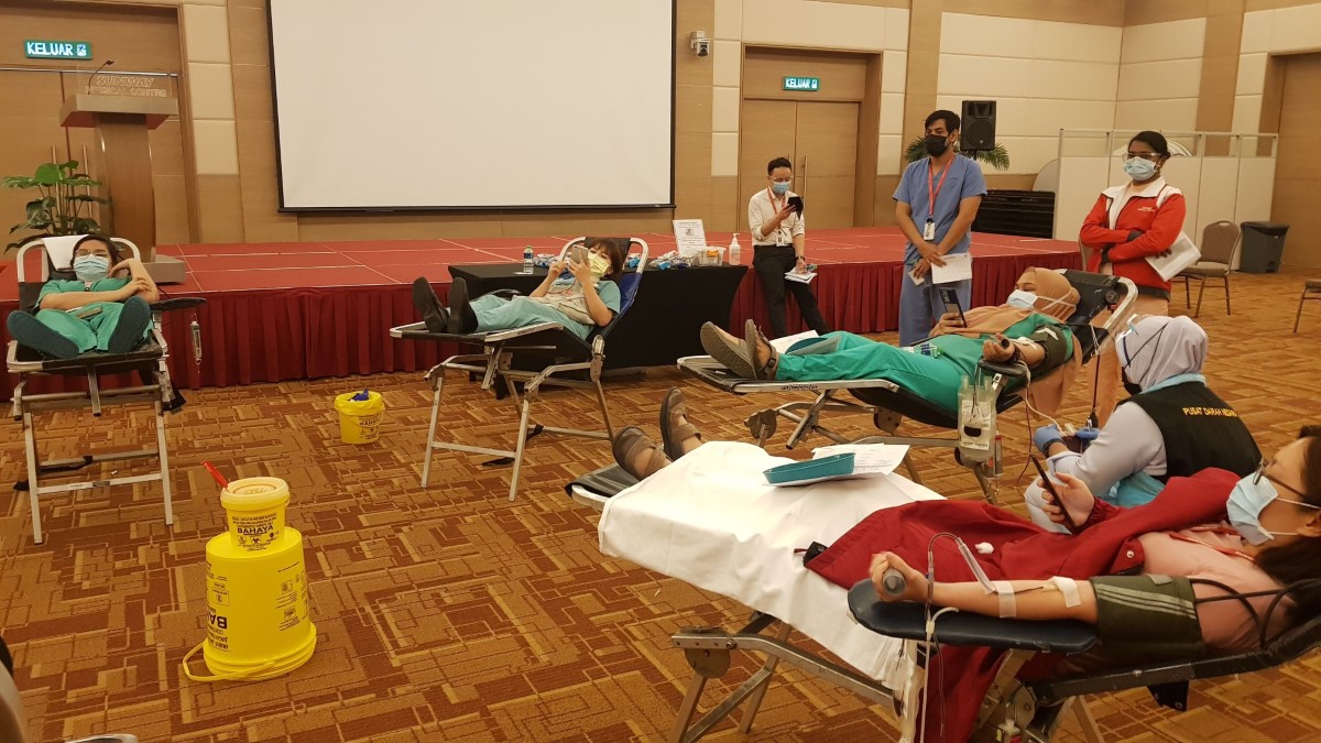 A wide shot of a number of blood donors dressed in nurse uniforms all propped up on recliner beds during a blood donation drive organised within SunMed Convention Centre