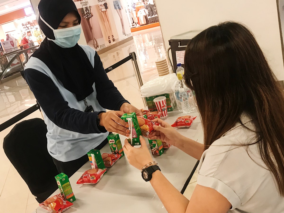 A mid shot of a Muslim female wearing surgical mask handing over boxed beverage and packet of muffin to a female blood donor after the session