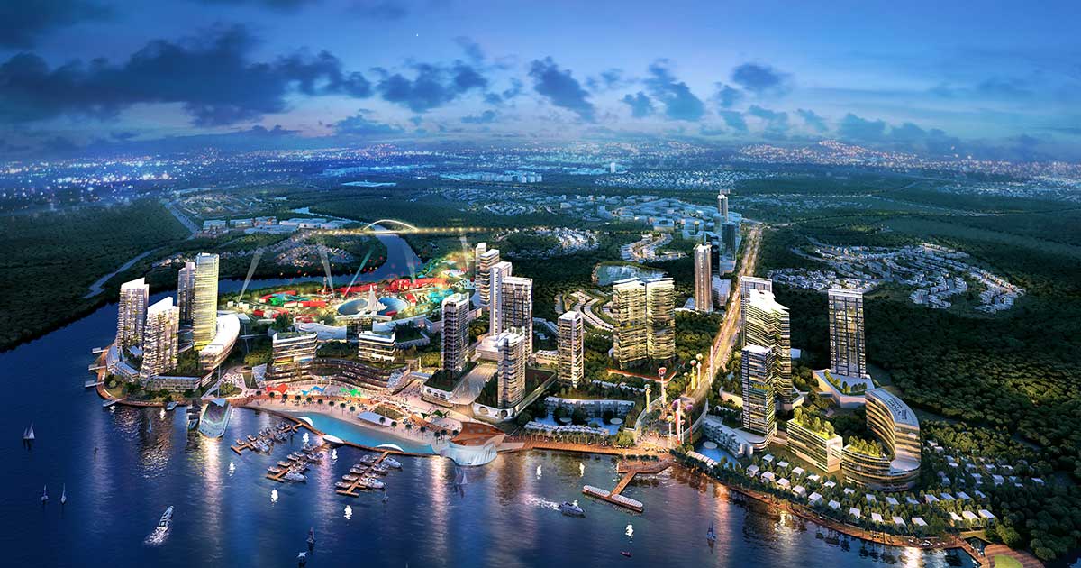 A bird’s eye view of Sunway City Iskandar Puteri at dusk, featuring brightly lit skyscapers which illuminates the dense greeneries surrounding It, reflected on the Straits of Johor and darkening skyline in the horizon