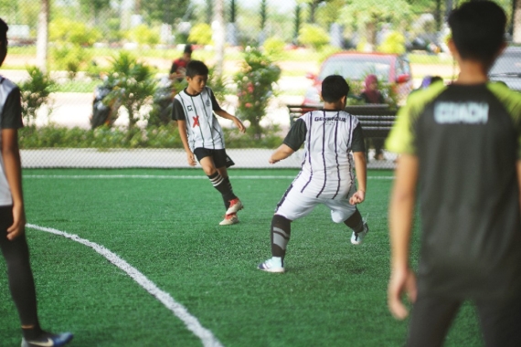 A wide shot of several boys playing futsal in an indoor court, each dressed in striped jerseys, shorts, knee-high socks and futsal shoes.