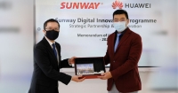 A mid-wide shot of Sunway Group CEO of digital & strategic investments, Evan Cheah, alongside Huawei Malaysia CEO Michael Yuan, both in masks, glasses and suits, with each holding one end of the commemorative plaque marking the Sunway x Huawei Strategic Partnership & Collaboration