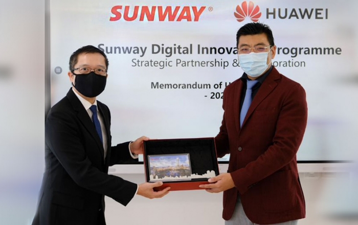 A mid-wide shot of Sunway Group CEO of digital & strategic investments, Evan Cheah, alongside Huawei Malaysia CEO Michael Yuan, both in masks, glasses and suits, with each holding one end of the commemorative plaque marking the Sunway x Huawei Strategic Partnership & Collaboration