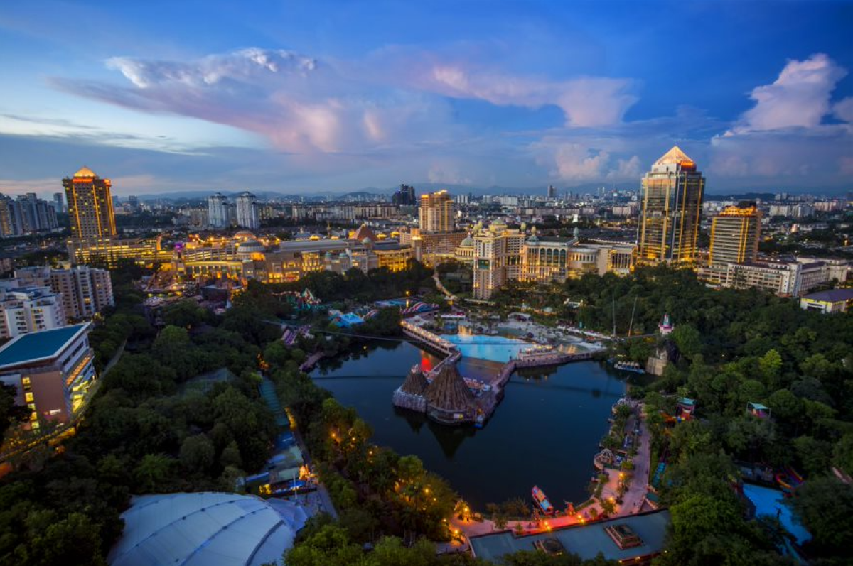 A wide angle shot of Sunway City Kuala Lumpur at dusk, featuring Sunway Lagoon right in the middle, surrounded by lush greenscape and lit city skyline