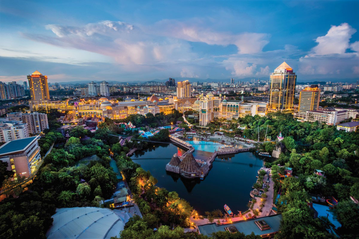 An aerial view of present-day Sunway Lagoon Theme Park at dusk, surrounded by lush greeneries and lit city skylines.