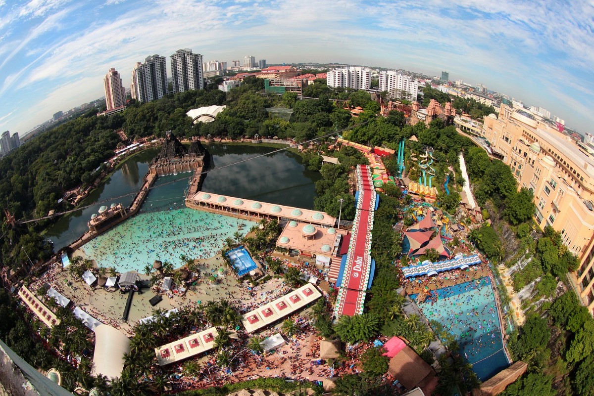 A birds-eye view of Sunway Lagoon Theme Park at mid-day, well-patronised by theme park goers under a clear and sunny sky.