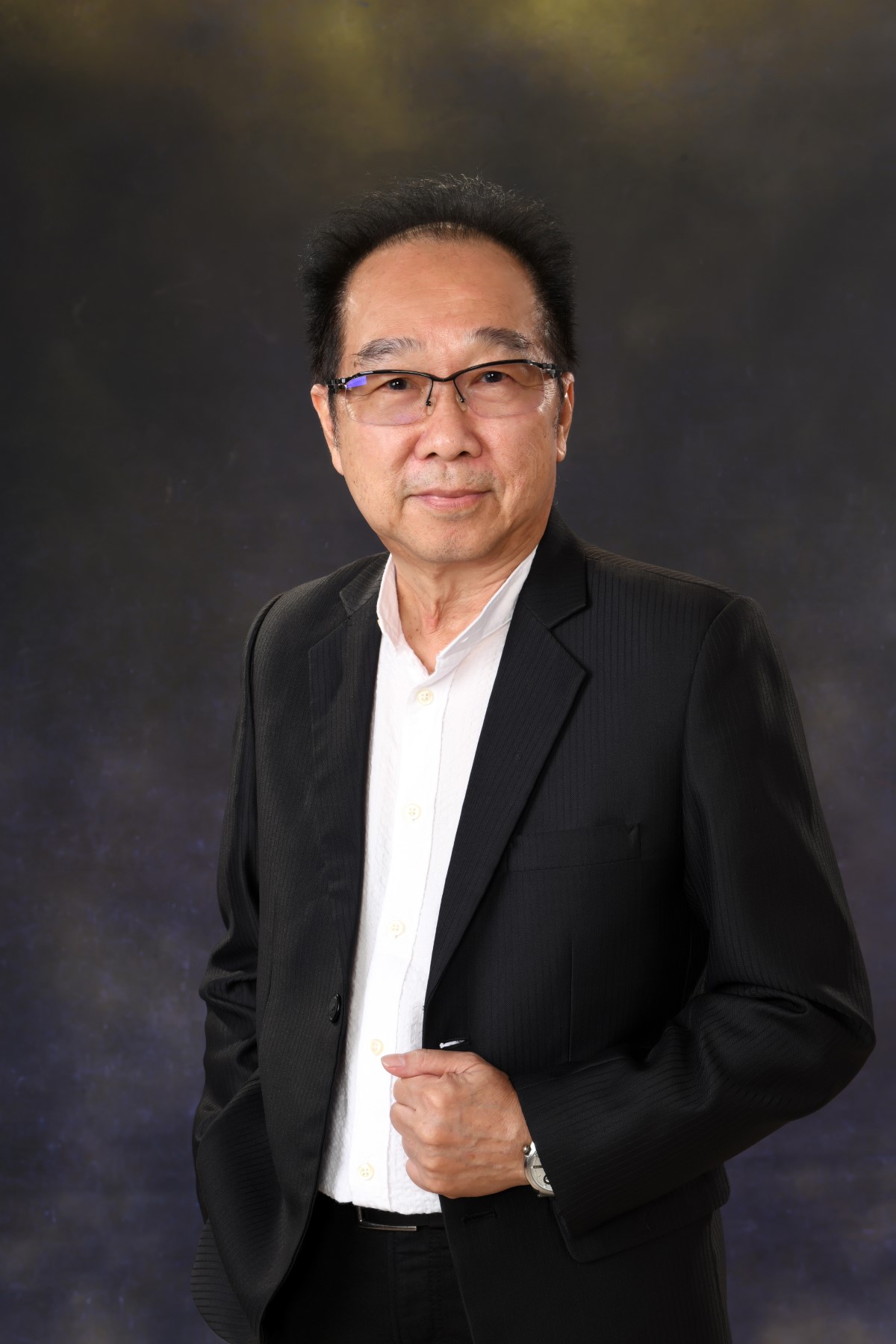 A mid-wide portrait of Sunway design director Nelson Yong, standing with one hand tucked in his pocket and another clasping the edge of his blazer, fronting a charcoal grey backdrop.