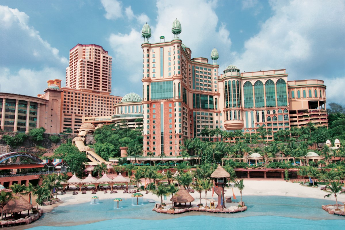 An aerial view of present-day Sunway Resort with its apricot façade, bright teal glasses and gold trims, surrounded by lush tropical greeneries and clear, blue waters.