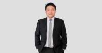 A portrait medium-shot of Sunway Group chief information officer Kevin Khoo Min Sinn, smirking at the camera with both hands tucked into his pants pocket, dressed in clasic black suit and a grey tie