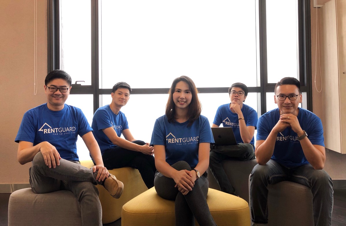 A medium full shot of RentGuard’s team of five comprising four males and one female – all wearing their signature blue tee shirt, seated in front of a wide window with bright daylight pouring in, led by co-founder and CEO Jeff Tan.