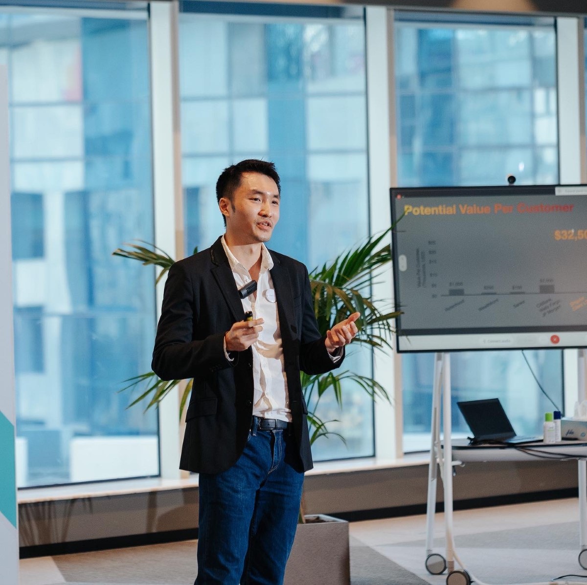 A medium full shot of Singular co-founder and CEO Terrence Hooi mid-presentation in front of a set of ceiling-to-floor windows.