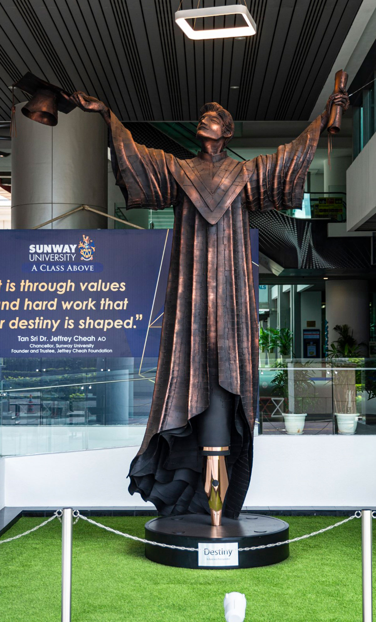 A bronze metal sculpture of a man holding a scroll and a graduation cap in each hand located at the lobby of Sunway University named ‘Destiny’.