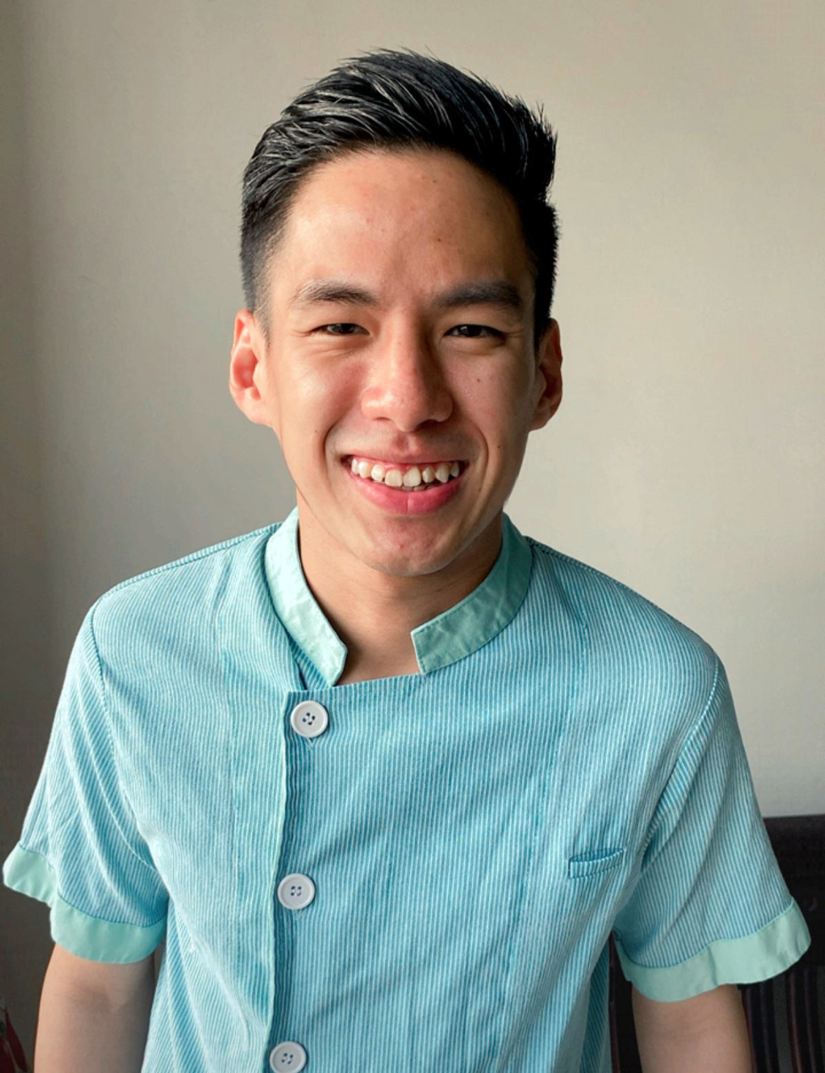 A half body shot of Jeremy Tan Shin Ming, a wound care nurse at Sunway Medical Centre smiling brightly in his blue nursing uniform.