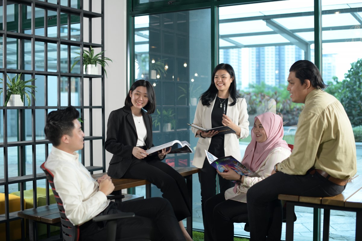 A medium full landscape shot of five Sunwayians from all walks of life, interacting with one another at interactive working spaces designed to promote employee engagement, holistic collaborations and improve workplace dynamics in general.
