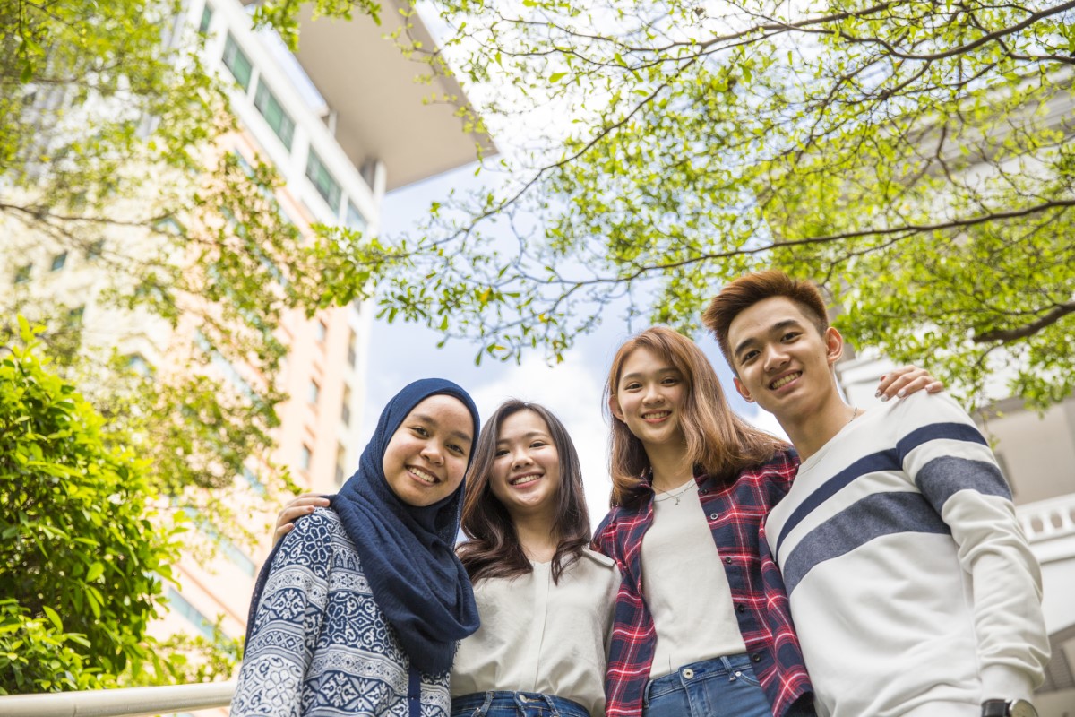 A low angled shot of students standing side by side with their arms around each other with a glimpse of the Sunway University building in the background.