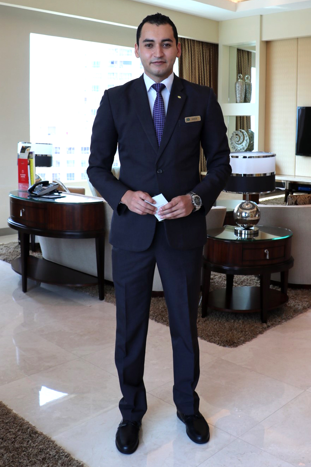 A full body shot of Mohammed Dawoud, a full-time guest relations manager dressed in a suit for work.