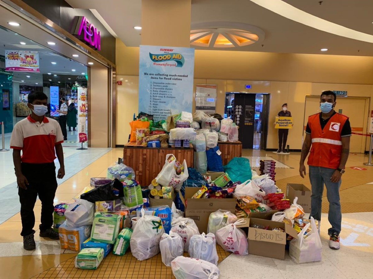 A full landscape shot of representative member of the Malaysian Red Crescent Society (MRC) in uniform and face masks posing by a mountain of essential necessities graciously donated by the public to aid Malaysian flood victims through the Sunway Malls Food Bank