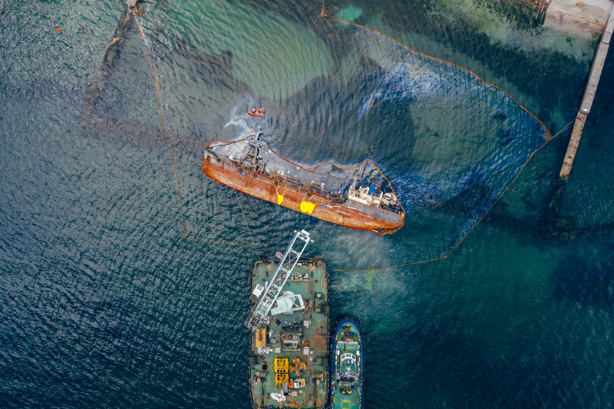 A drone shot of oil spill in the ocean. With the boat and oil rig leaking out black liquid.