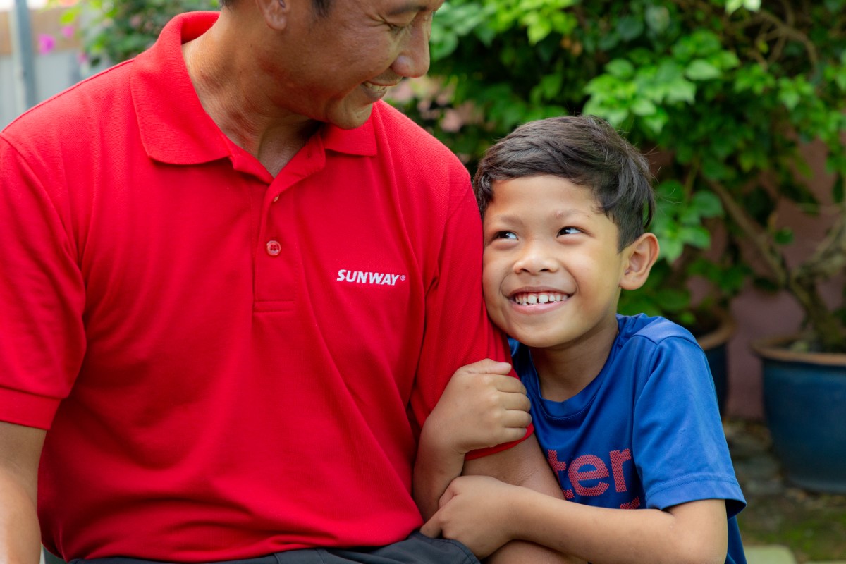 A tight medium landscape shot of a male child tightly hugging the left arm of Sunway Lost World of Tambun general manager Nurul Nuzairi bin Mohd Azahari as they look fondly at one another