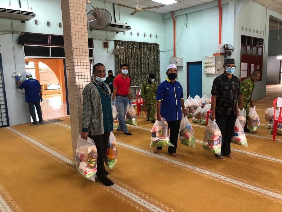 A full landscape shot of Sunway Lost World of Tambun general manager Nurul Nuzairi bin Mohd Azahari in signature red polo tee and face mask among a group of male volunteers carrying heavy bags of groceries and necessities for flood-hit residents in Teluk Intan