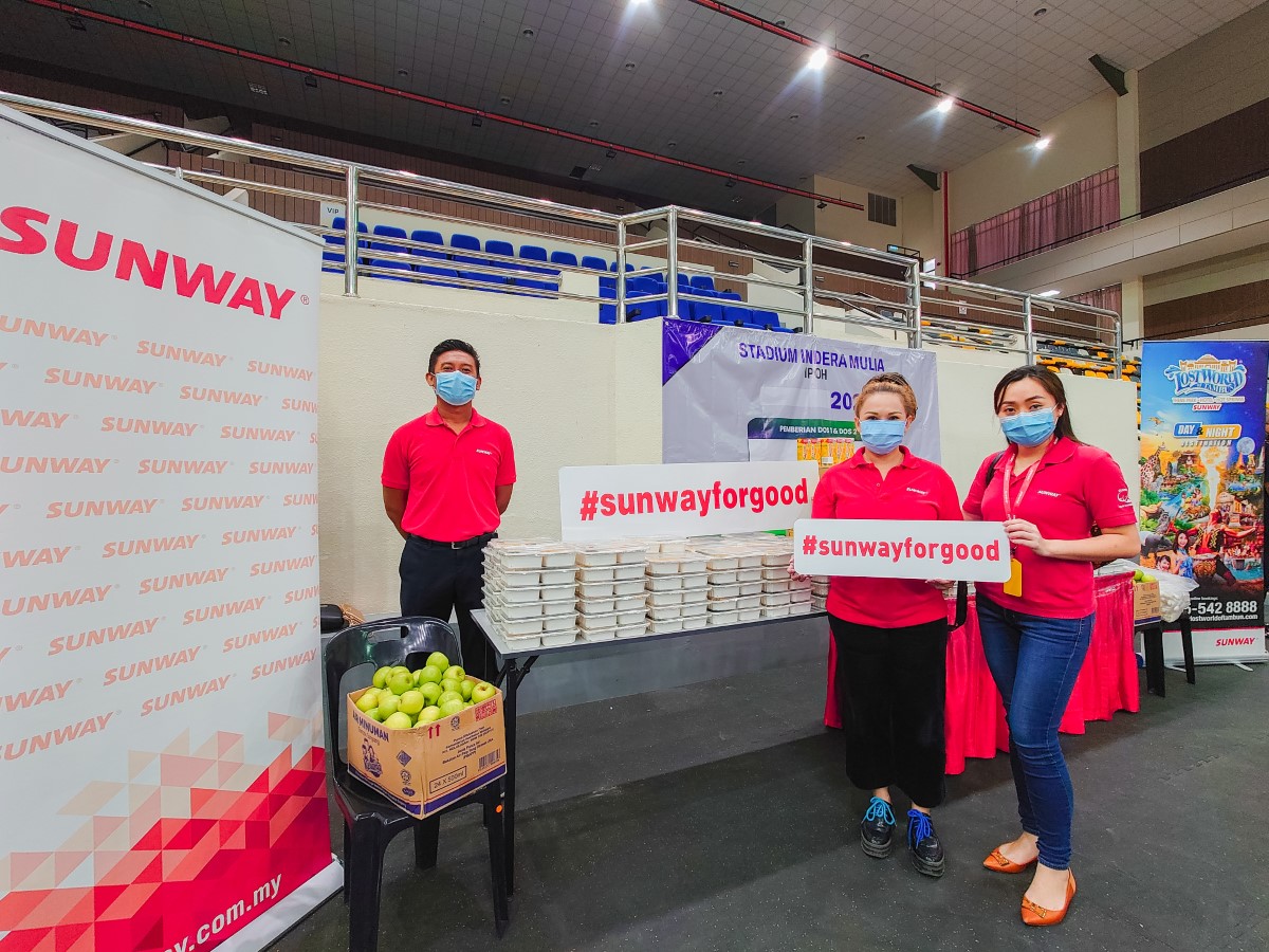 A full landscape shot of Sunwayians in signature red polo tee and face mask among multiple #SunwayforGood banners and rows of pre-packed meals to be distributed to frontline workers during MCO 3.0 in Ipoh