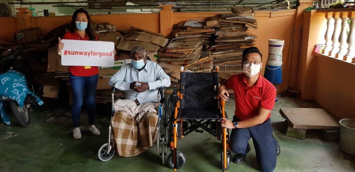 A full landscape shot of Susan (left) in signature red polo tee and face mask propping up our #SunwayforGood banner after delivering wheelchairs to beneficiaries in the northern region