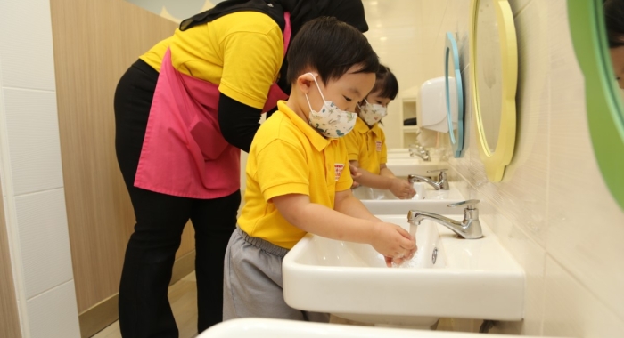 A full landscape shot of a Sunway Little Sunshine homeroom teacher helping toddlers wash their hands after interactive activities and before mealtime