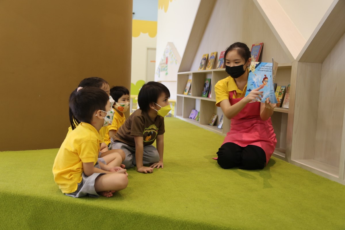 A full landscape shot of a Sunway Little Sunshine homeroom teacher reading aloud to toddlers by the centre’s designated Reading Tree