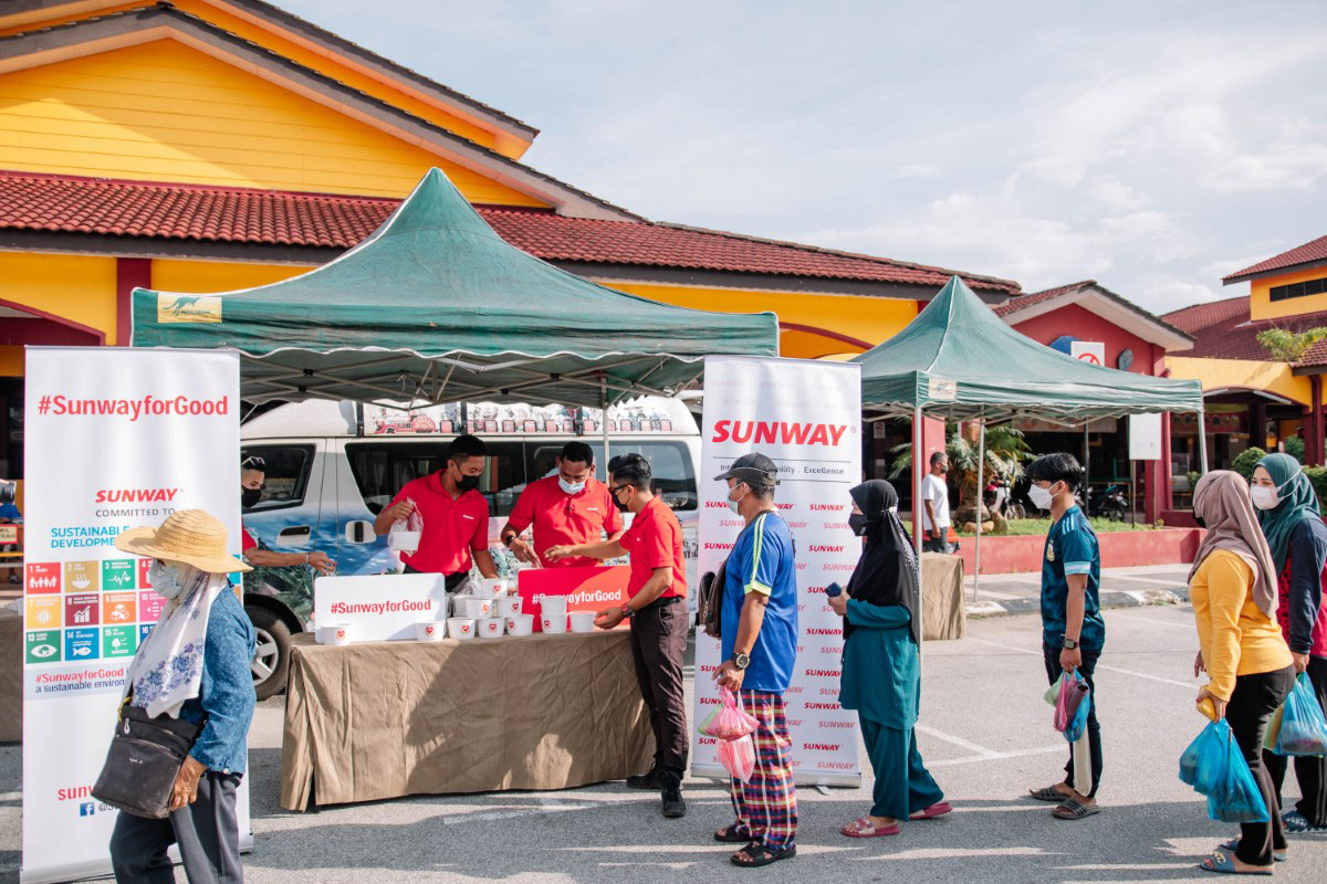 A full landscape shot of Sunwayians donning signature red polo tees distributing bubur lambuk to local communities as part of our #SunwayforGood Raya Cheer 2022 at Dataran Lenggong, Perak