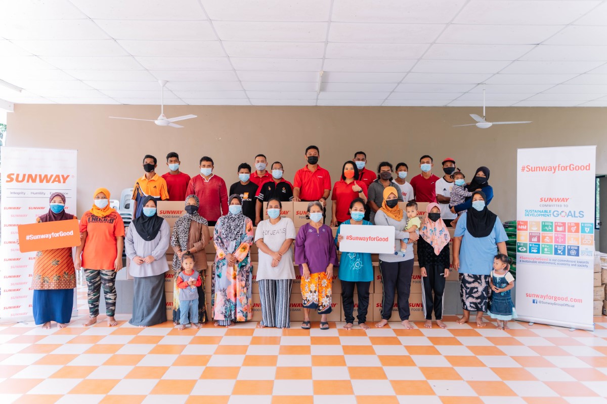 A full landscape shot of the Orang Asal community in Kampung Sg. Choh alongside Sunwayians donning signature red polo tees in the town’s multi-purpose hall after groceries and essential goods distribution