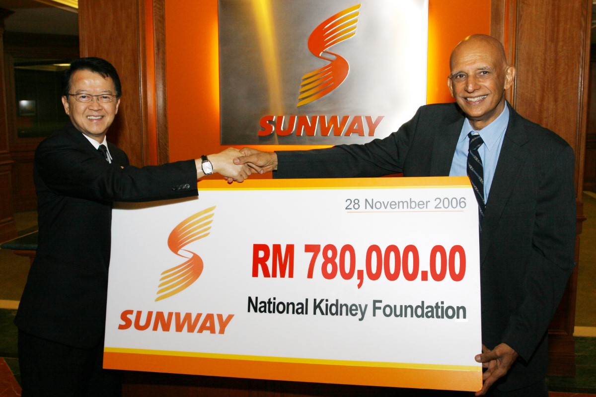 Tan Sri Dr. Jeffrey Cheah handing a mock cheque with the second logo to the National Kidney Foundation, and shaking hands with the Sunway logo in the background
