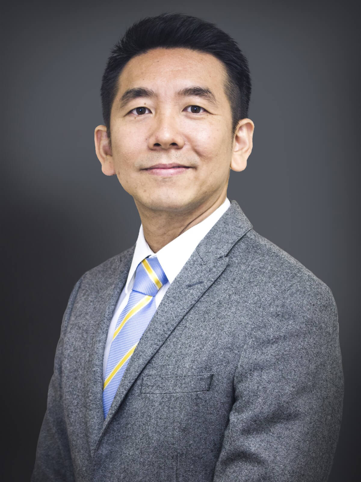 Dr. Kow’s portrait shot, in a grey blazer and blue and gold tie