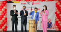 Sarawak Deputy Premier Datuk Seri Dr Sim Kui Hian hitting the drum alongside Tan Sri Dr. Jeffrey Cheah as the foreground, with the Sunway TCM Centre and Sunway Fertility Centre launch backdrop decorated with red balloons in the background