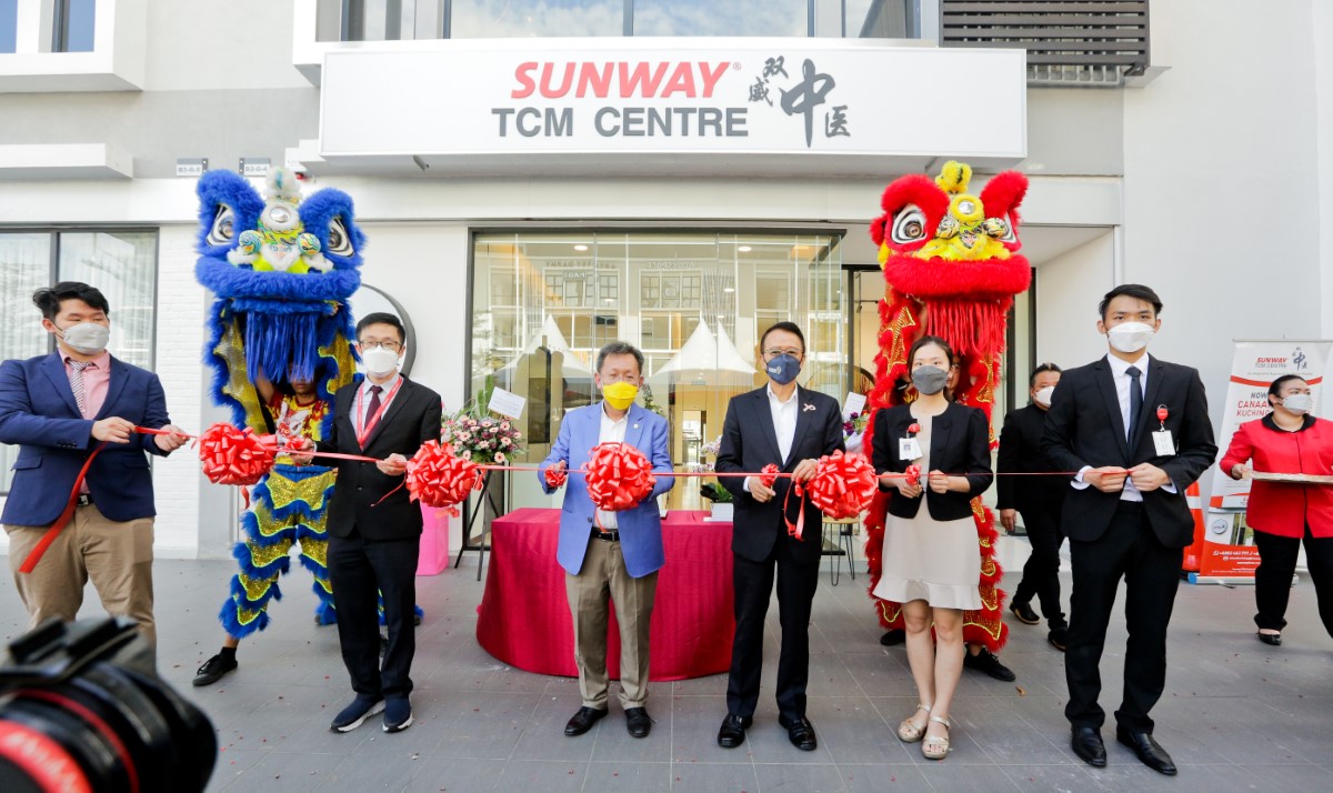 Sarawak Deputy Premier Datuk Seri Dr Sim Kui Hian clad in light blue blazer in the middle, alongside Tan Sri Dr. Jeffrey Cheah clad in black suit in the middle, alongside Sunway staff officiating the event. Holding red ribbon in front of the Sunway TCM Centre shop lot, flanked by lion dancers.