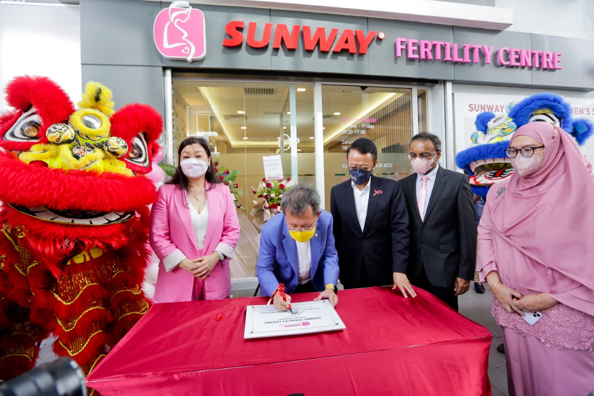 Sarawak Deputy Premier Datuk Seri Dr Sim Kui Hian in the midst of his signature, witnessed by Tan Sri Dr. Jeffrey Cheah in front of Sunway Fertility Centre. Flanked by Sunway staff and a lion dancer.