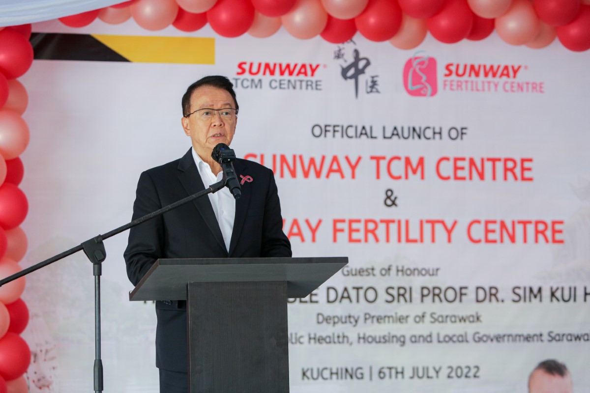 Tan Sri Dr. Jeffrey Cheah giving a speech in the foreground, with the Sunway TCM Centre and Sunway Fertility Centre launch backdrop decorated with red balloons in the background