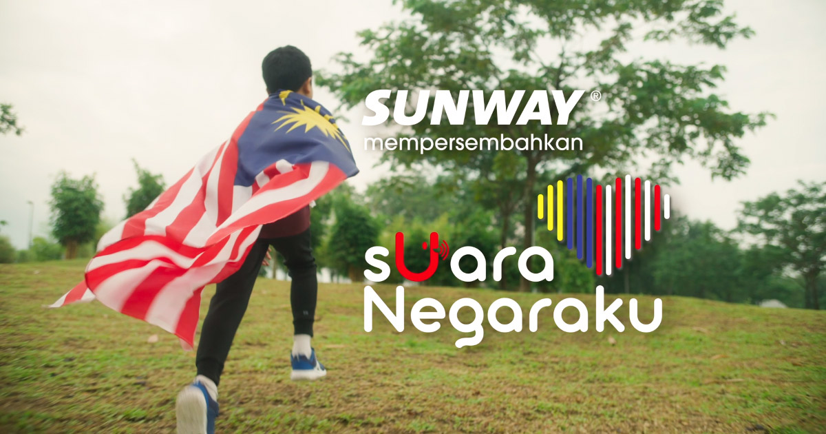 A boy running up a hill with the Malaysian flag draped across his back, with trees in the background. Also features the Sunway logo, ”Suara Negaraku” tagline and the heart-shaped Malaysia-themed key visual.