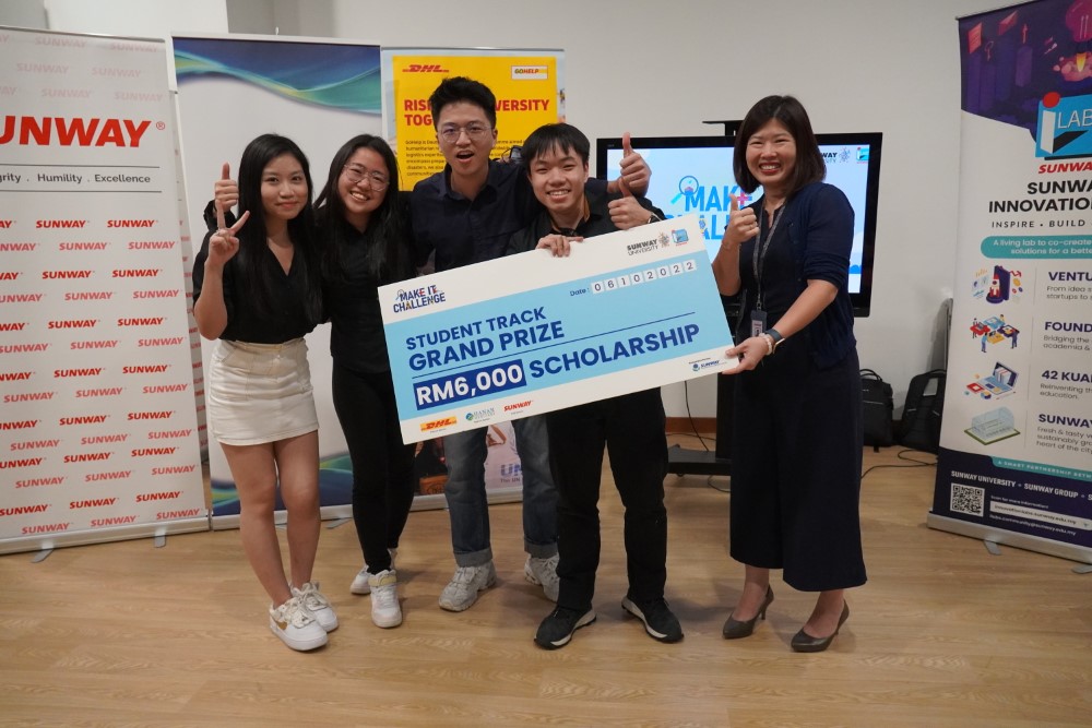 Sunway University students posing with the mock cheque as grand prize winner of Make It Challenge Student Track, in front of Sunway, Sunway iLabs and DHL banners, with iLabs Foundry Director Karen Lau Kai Zhia alongside them.