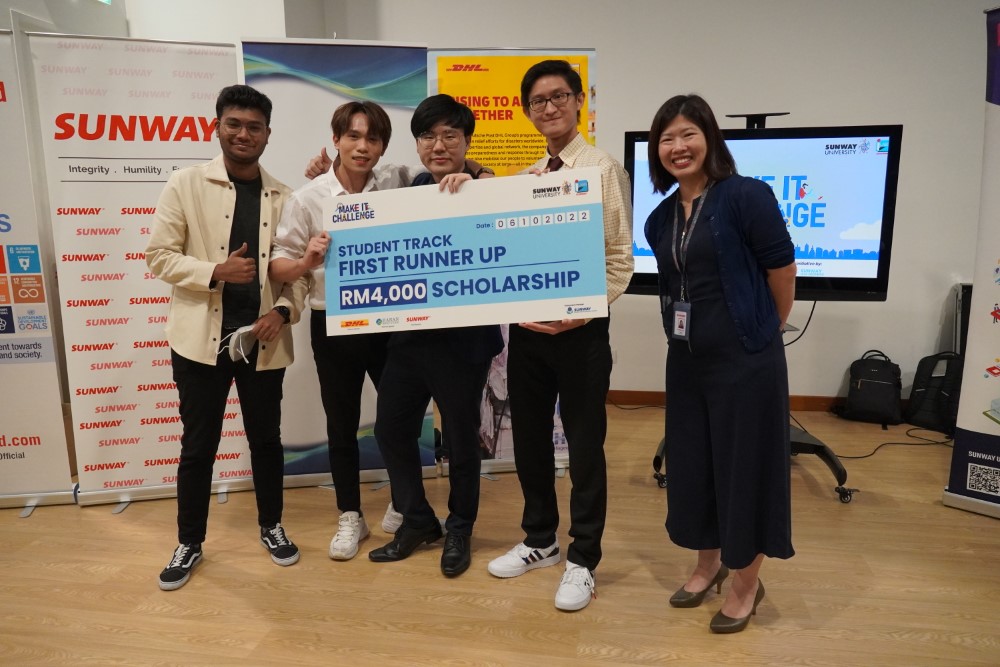 Sunway University students posing with the mock cheque as first runner-ups of Make It Challenge Student Track, in front of Sunway, Sunway iLabs and DHL banners, with iLabs Foundry Director Karen Lau Kai Zhia alongside them.