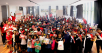 A group photo containing some 140 children from Johor, alongside Sunway staff clad in Sunway red. The photo was taken in a well-lit hall.