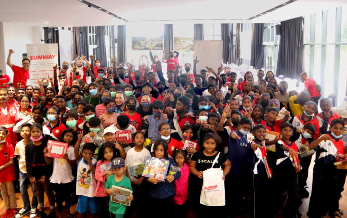 A group photo containing some 140 children from Johor, alongside Sunway staff clad in Sunway red. The photo was taken in a well-lit hall.