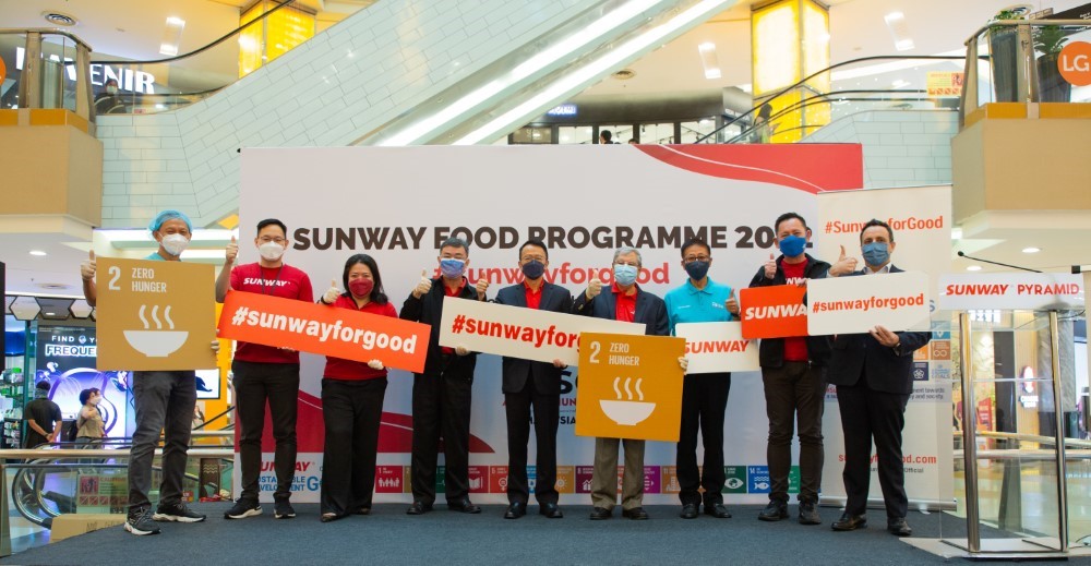 A full landscape shot of Sunway leaders and key stakeholders holding up #SunwayforGood and SDGs signs respectively during the launch of Sunway Meal Pack-a-Thon 2022.