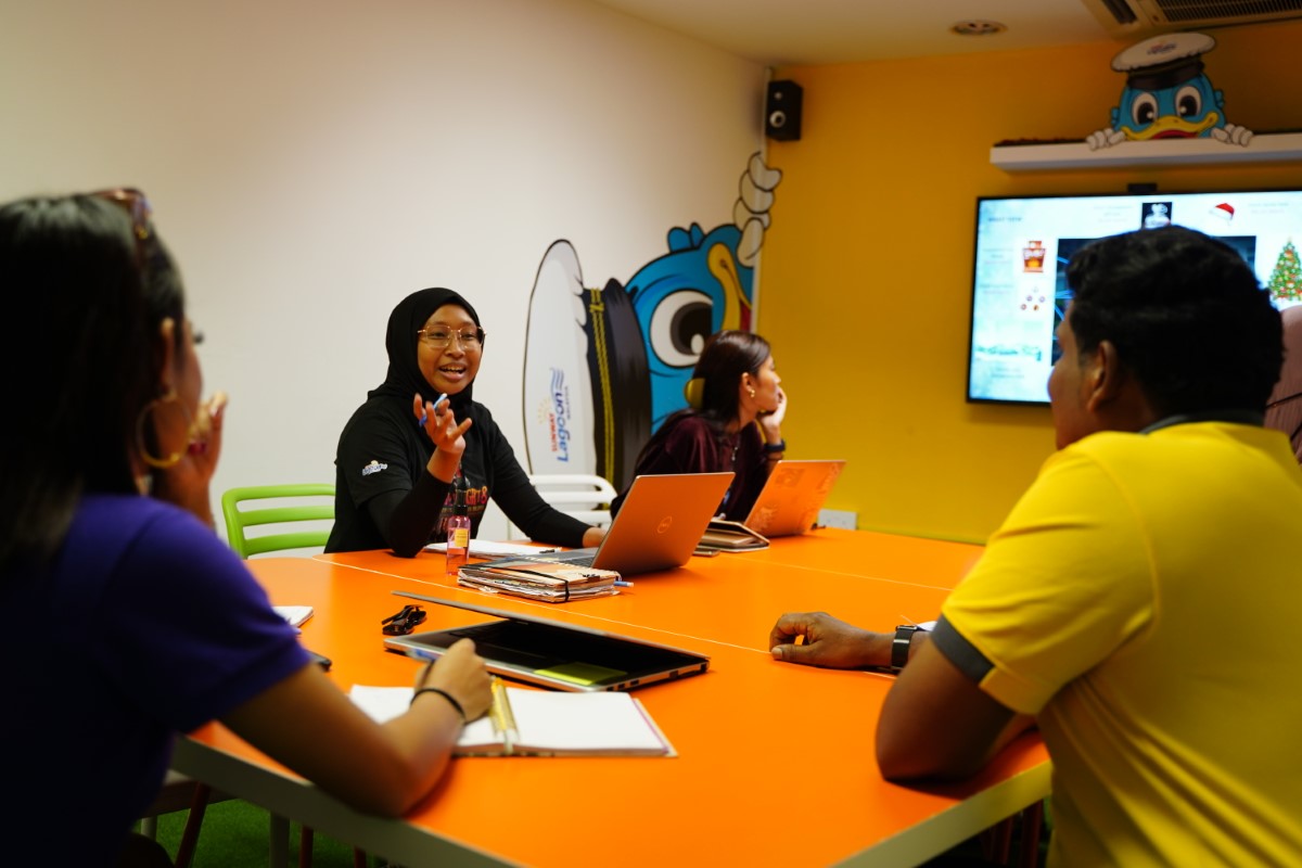 Mid shot of Aishah regrouping with the team in the Sunway Lagoon meeting room.