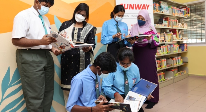 A medium full landscape shot of students and teachers leafing through pages of donated books in a newly-furnished library at Sekolah Menengah Kebangsaan Yaacob Latif in Cheras, Kuala Lumpur.